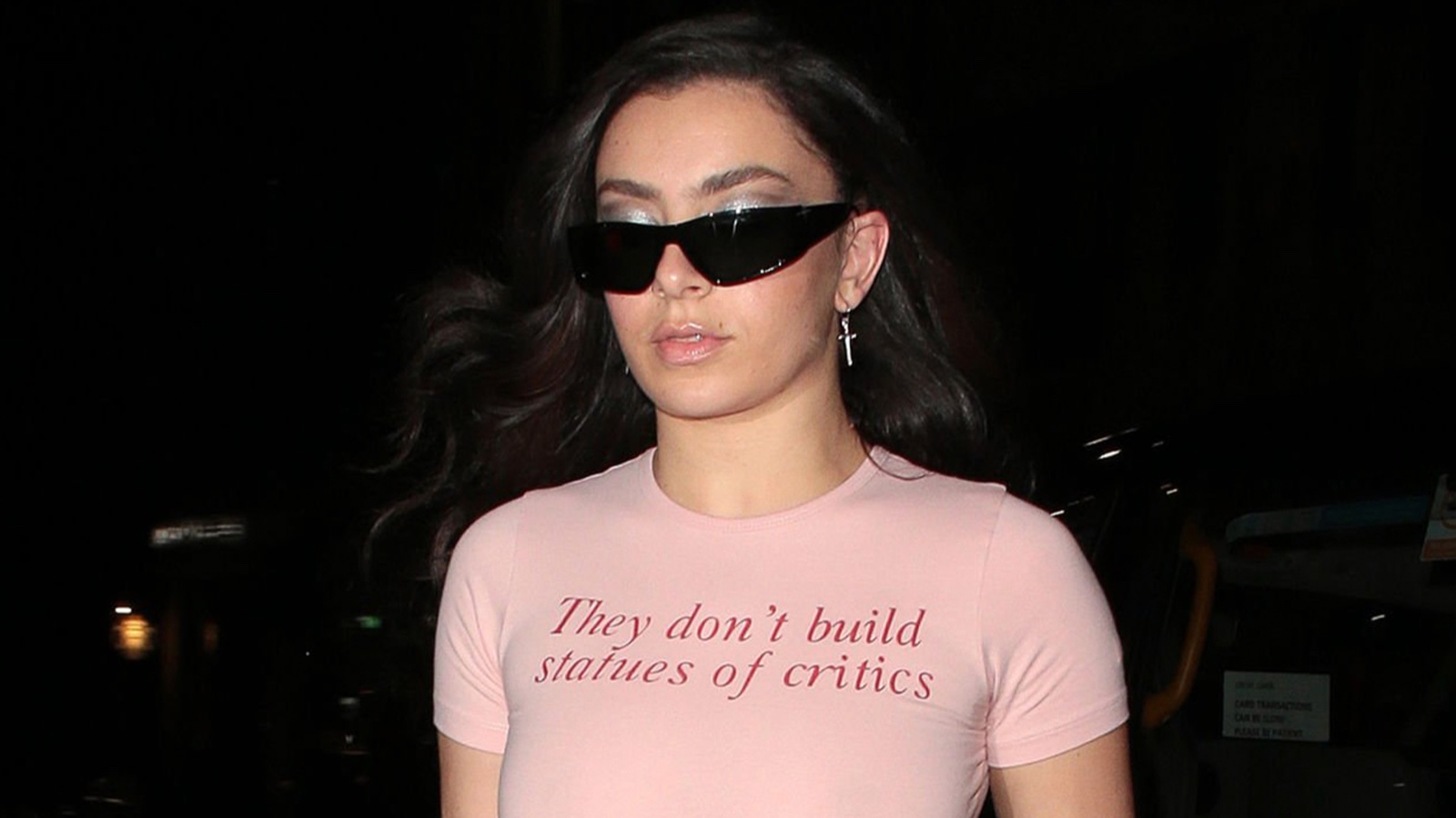 Charli XCX photographed in a pink t-shirt reading 'They don't build statues of critics.'